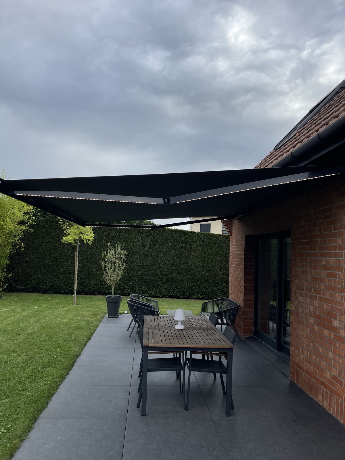 Store banne anthracite déployé au-dessus d'une terrasse aménagée